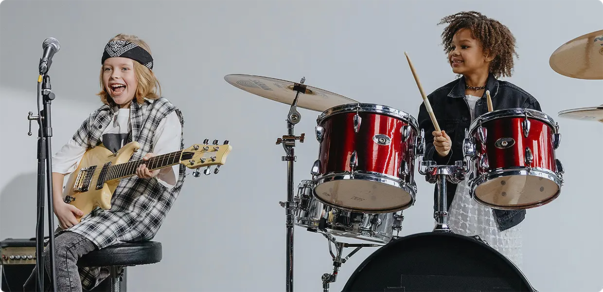 Two children performing together on stage playing electric guitar and drums