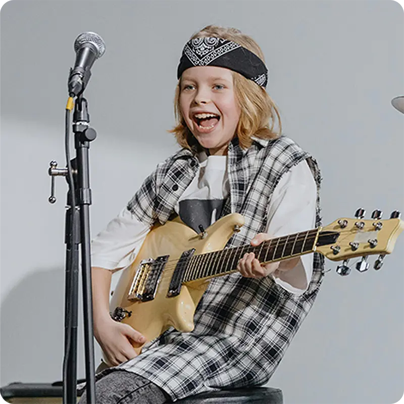 Two children performing together on stage playing electric guitar and drums